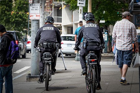 two police officers riding bicylces on city sidewalk