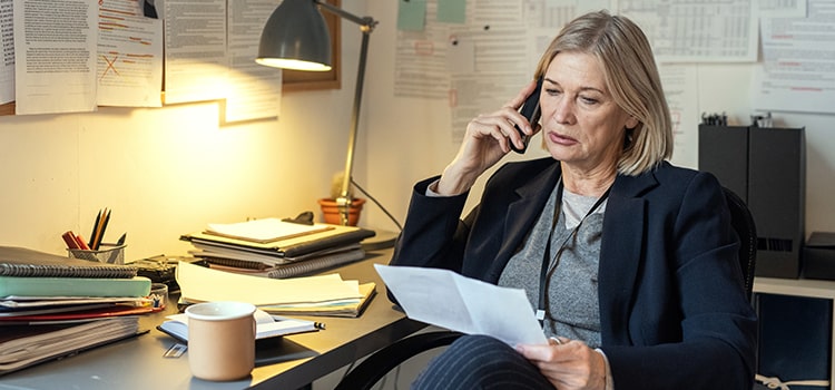 investigator on phone holding piece of paper seated at messy desk