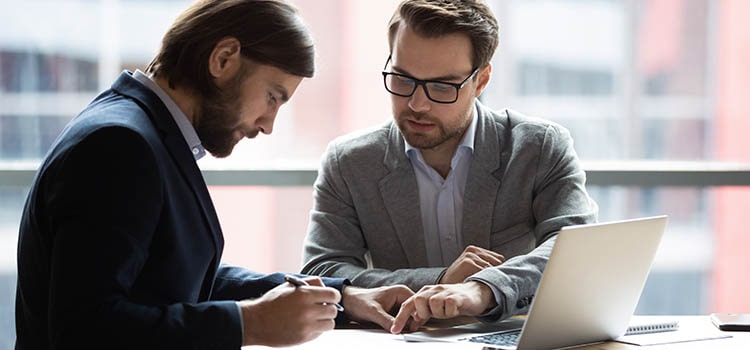 two suited professionals discuss paperwork in meeting room
