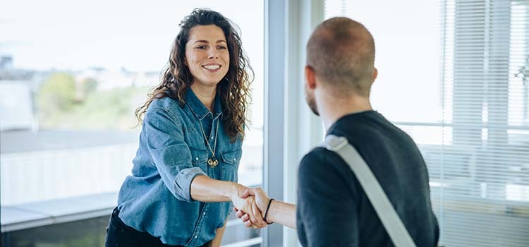 two people shake hands leaning across conference table