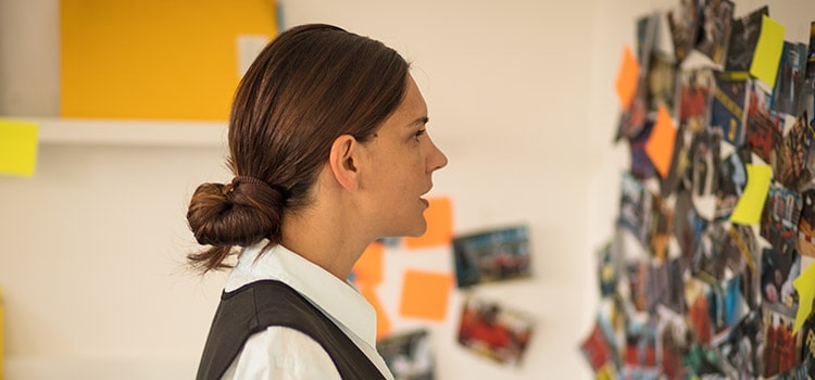 professional in black vest looks at bulletin board of crime images