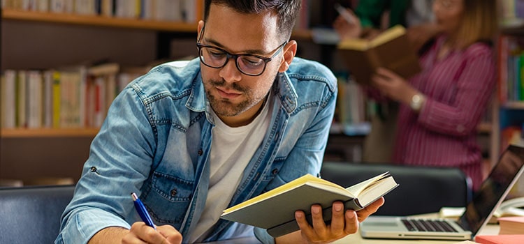 student takes notes from books in corner of library