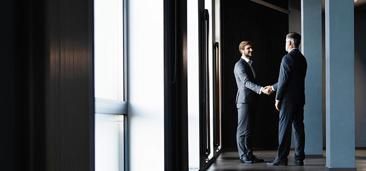 two professionals in suits shake hands in open hallway