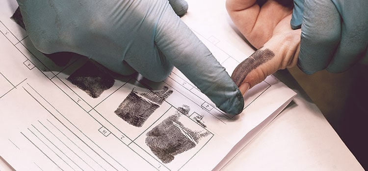 gloved hands guide inked fingers over fingerprint card