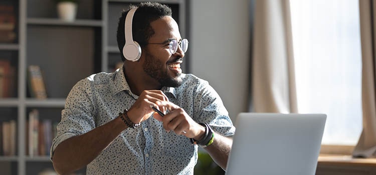 Person wearing headphones smiles looking away from laptop screen