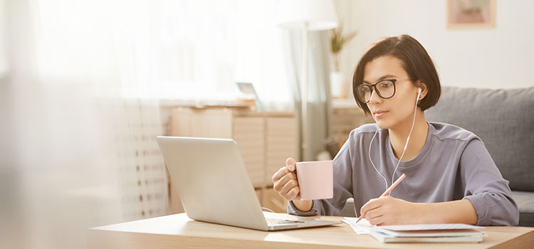 woman holding coffee cup on laptop taking transcription test with earbuds