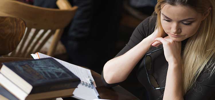 woman in college library studying with pile of books