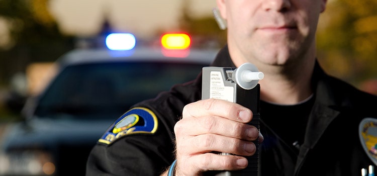 law officer standing in front of patrol car with lights on holds breathalizer tester up