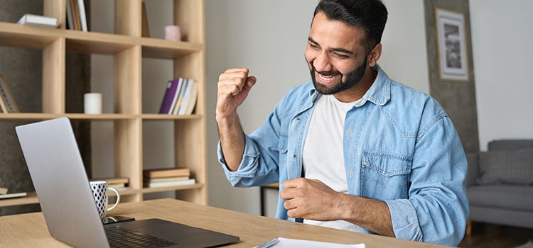 excited person seated at desk with laptop open after exam results are read