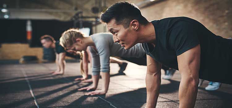 three people do pushups in a gym