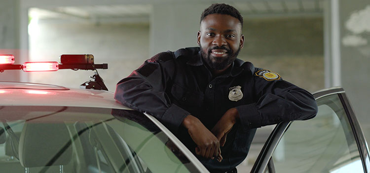 male police officer stands at his car and smiles