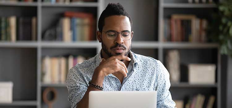 man sitting at desk does research on his laptop
