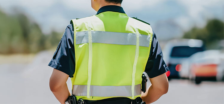 state trooper in safety vest helps reroute traffic after accident